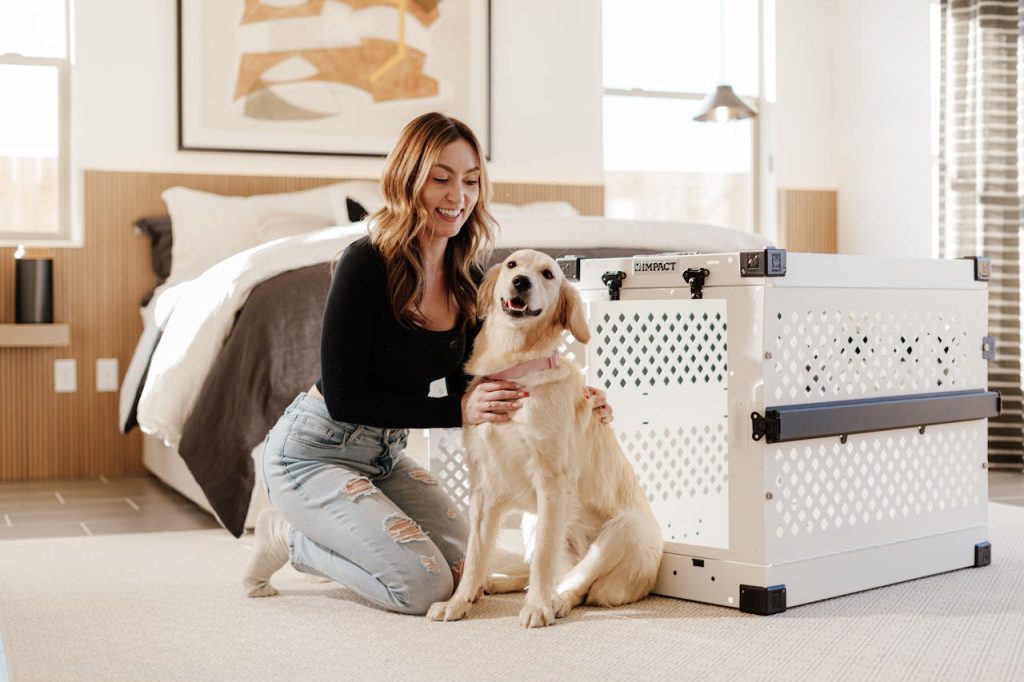 Woman enjoying time with her golden retriever beside a stylish dog crate in a bright bedroom.